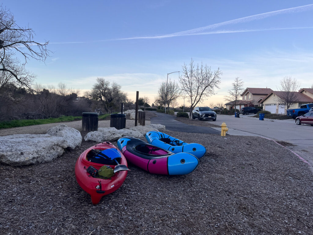 One kayak and two packrafts sit on the dirt in a neighborhood in Paso Robles as the sun sets